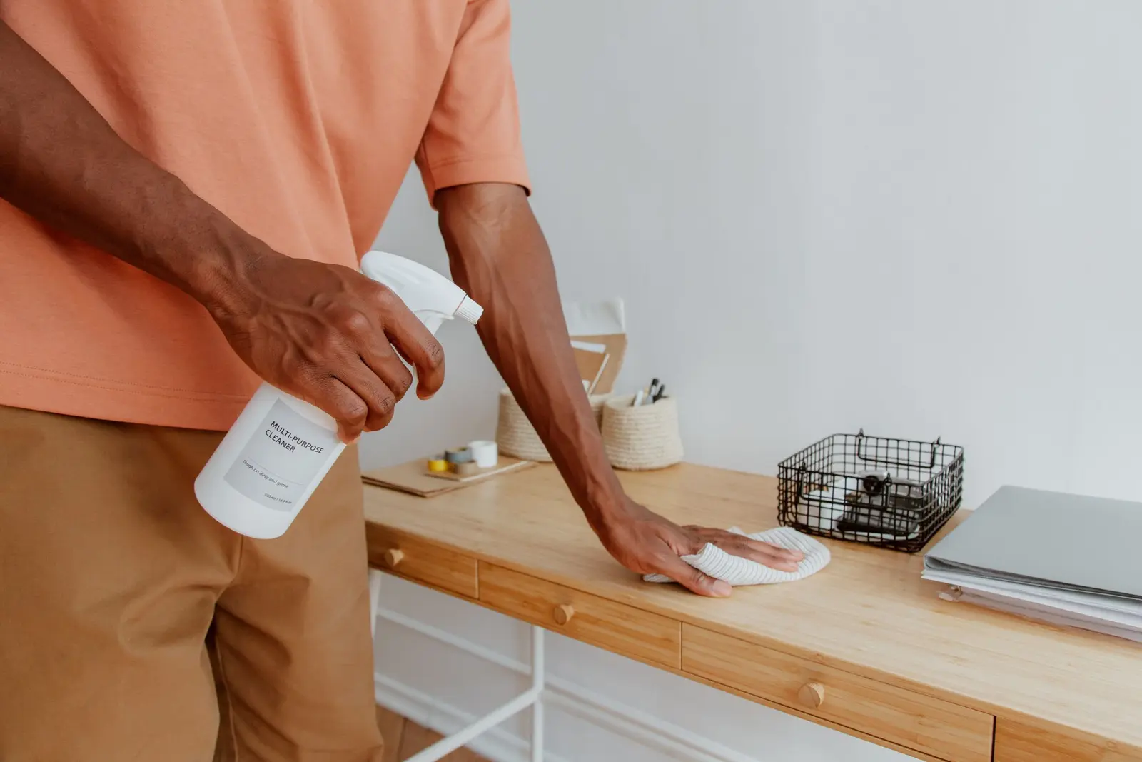 Person wiping down a wooden desk with a spray bottle and cloth