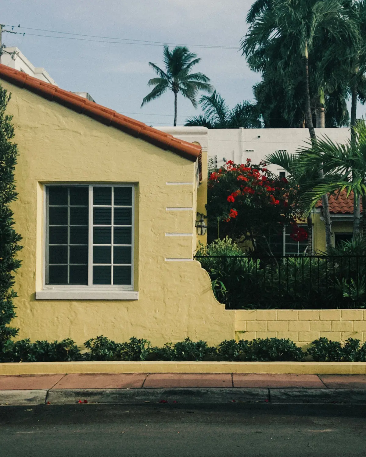 Yellow stucco Florida home with a white window and red flowers