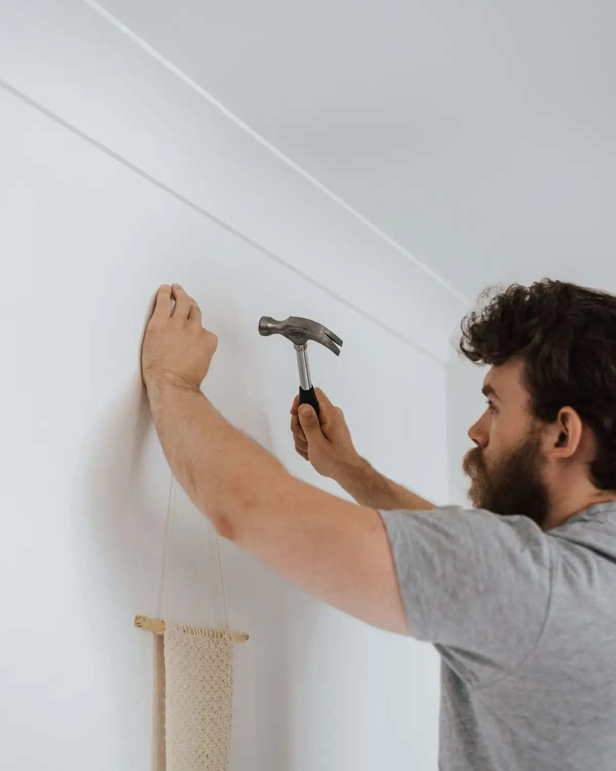 Handyman tapping a nail into a white wall with a hammer