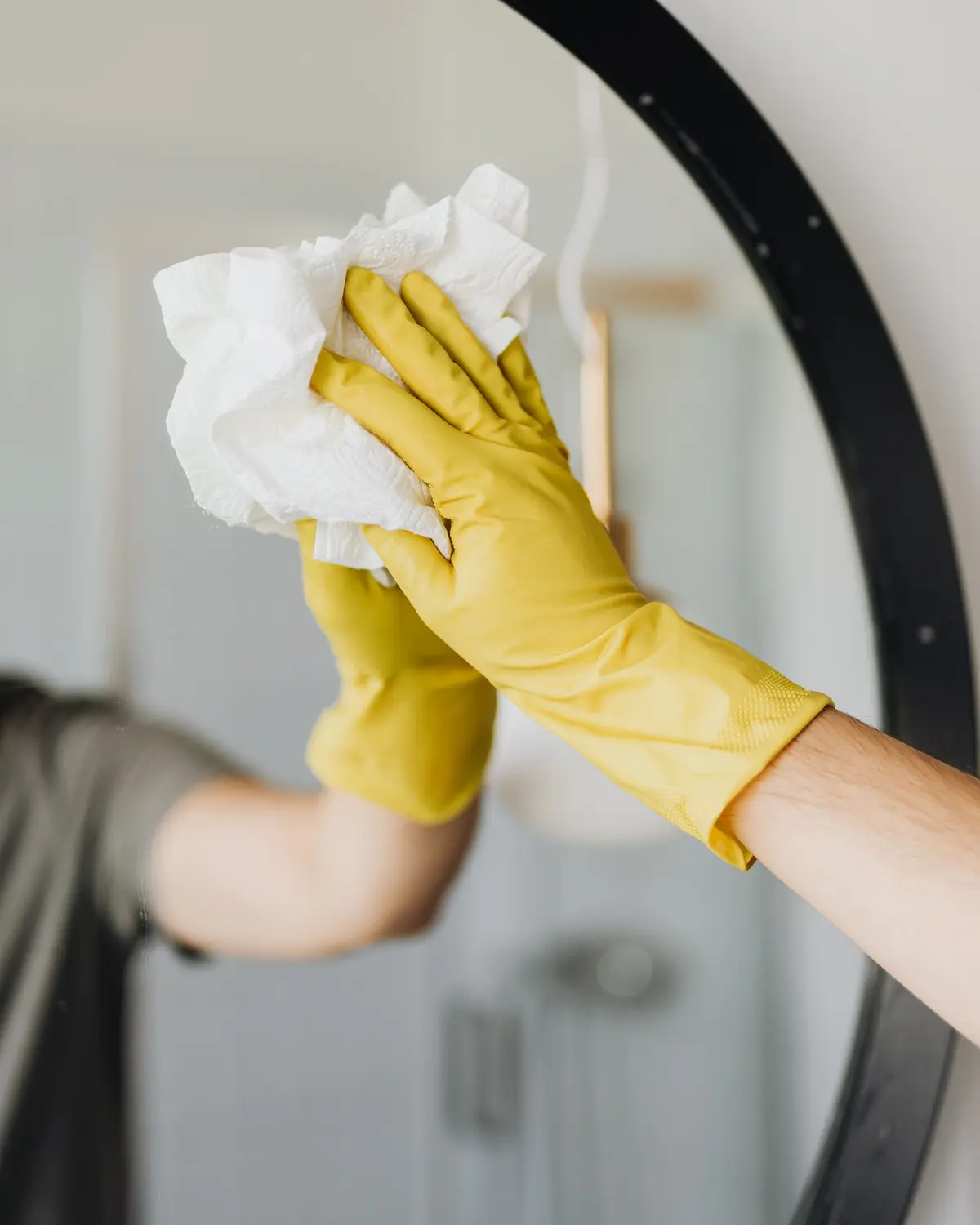 Yellow-gloved hand polishing a bathroom mirror