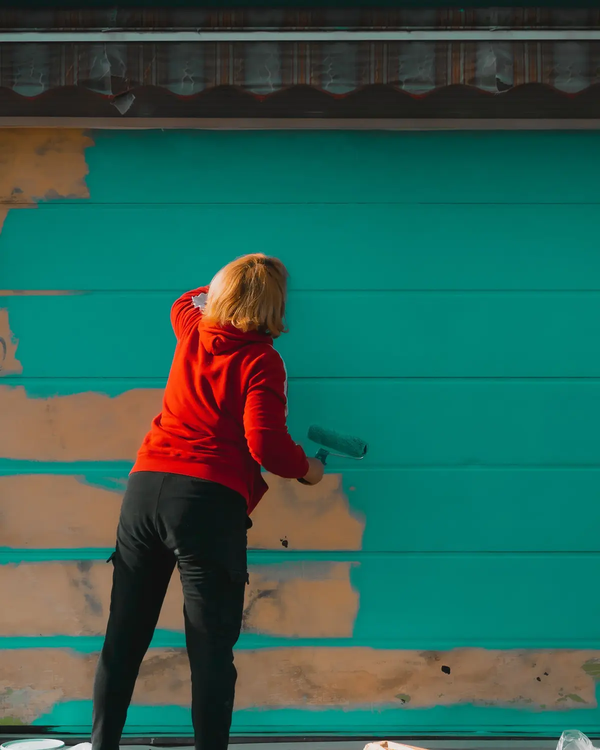 Painter rolling teal paint onto a wall