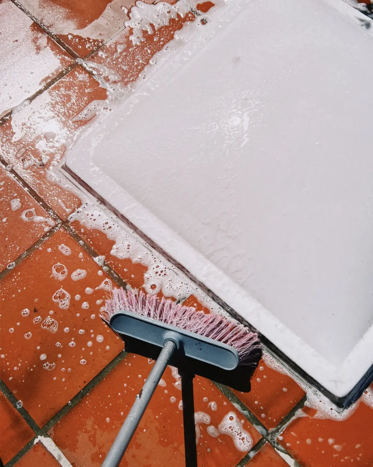Brush scrubbing soapy grout lines on a tiled floor